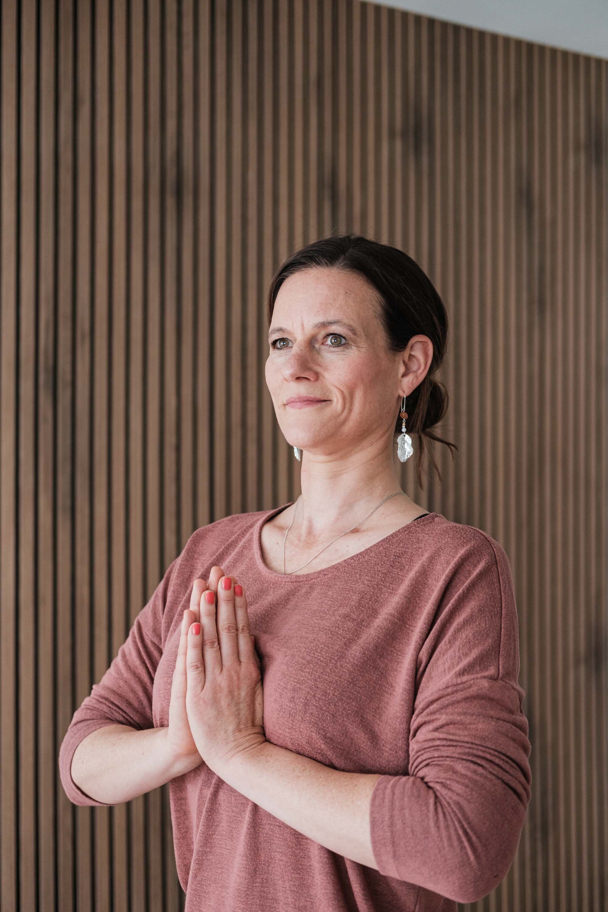 Ariane Grebenstein steht mit gefalteten Händen im Yogastudio